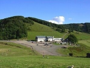 A rural landscape with a white building surrounded by green fields and hills. - Hotel le Rouge Gazon (Saint-Maurice-sur-Moselle)