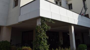 Un moderno edificio de hotel con un logotipo destacado, varios balcones y una zona de entrada cubierta con plantas en macetas.