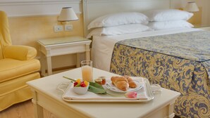 Una bandeja de desayuno ordenada con croissants, fruta y un vaso de zumo de naranja sobre una mesa blanca en una habitación de hotel.