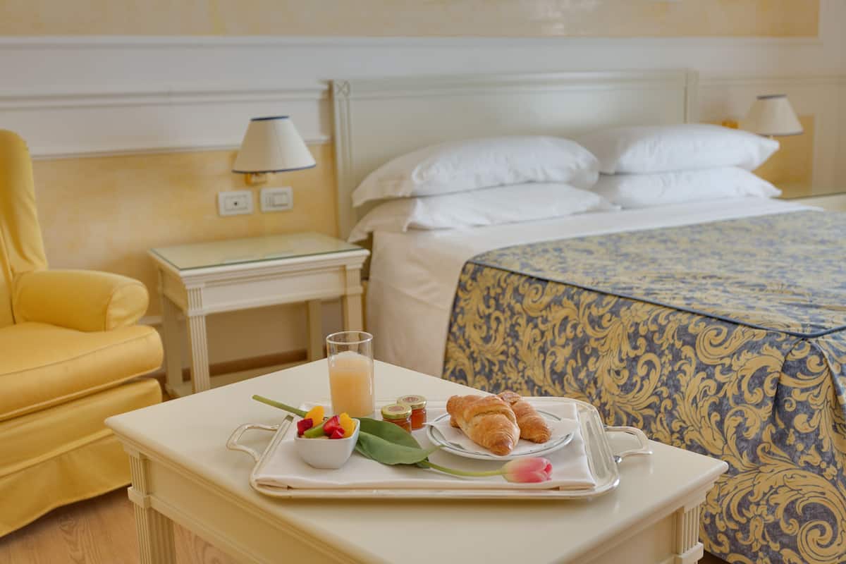 Una bandeja de desayuno ordenada con croissants, fruta y un vaso de zumo de naranja sobre una mesa blanca en una habitación de hotel.
