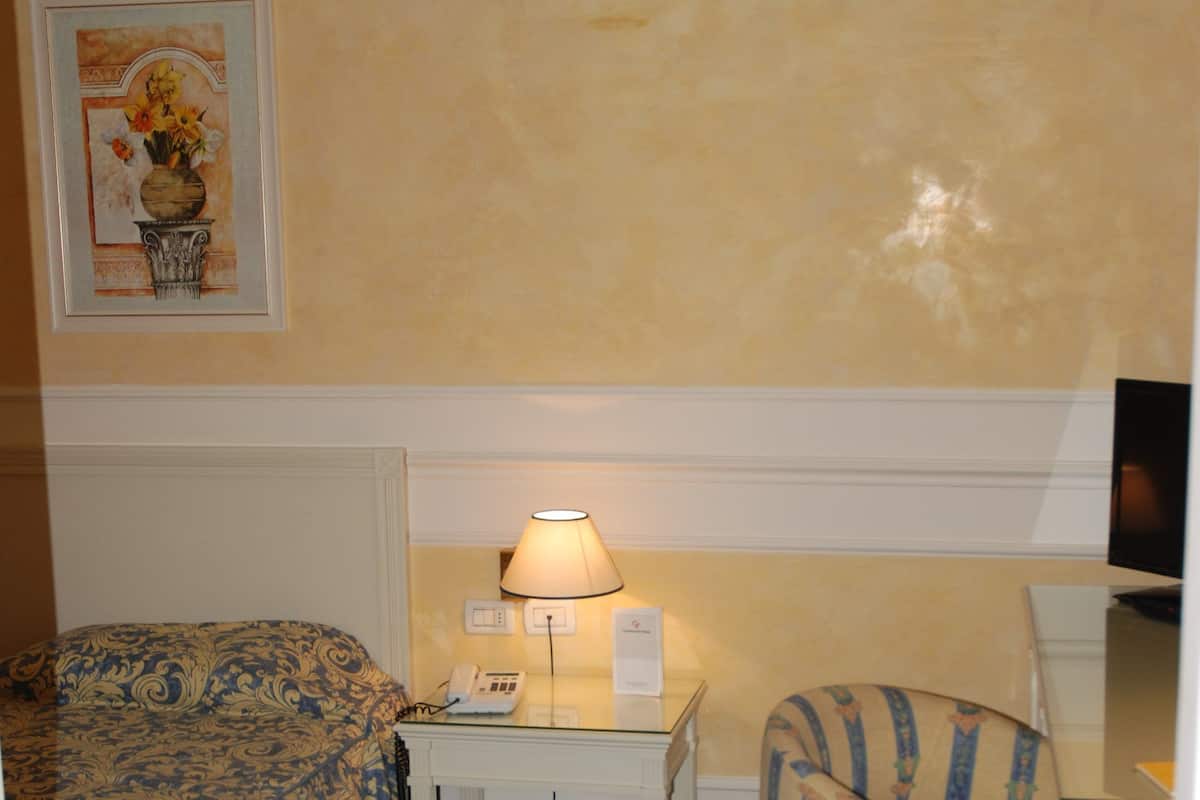 Habitación de hotel con cama, escritorio con lámpara, silla y un cuadro en la pared.