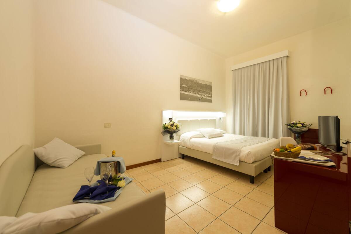 A hotel room with a bed, a sofa, a desk with a computer, and a window with curtains.