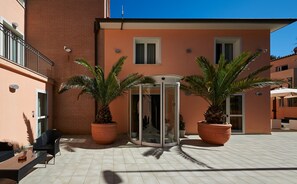 Entrada de hotel con puerta giratoria, palmeras en macetas y patio con baldosas.