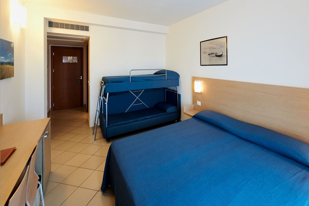 Una habitación de hotel con literas, una cama individual, un escritorio y una silla.