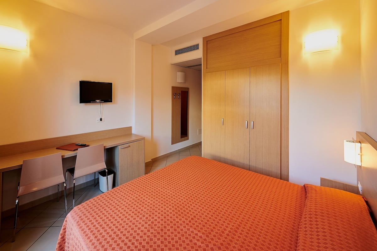Una habitación de hotel con cama, escritorio, silla, televisor y armario.