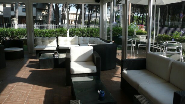 An outdoor patio area with seating arrangements including sofas and tables, surrounded by glass walls offering views of the surrounding area. - Bolgheri Marina Resort ex Varo Village (Bibbona)