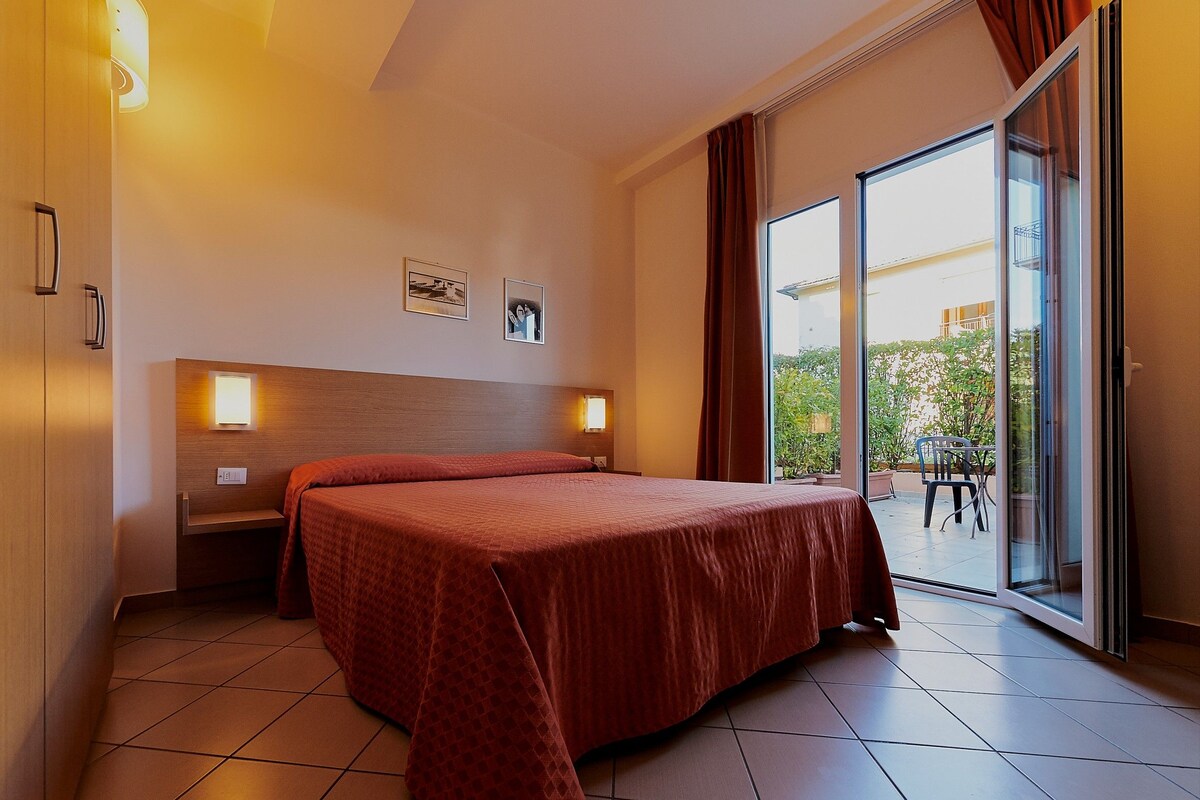 Habitación de hotel con cama, dos mesitas de noche, una ventana con cortinas y vistas al exterior.