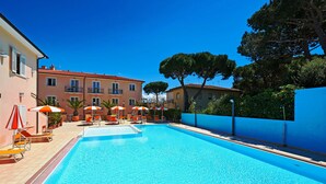 A swimming pool with lounge chairs and umbrellas, surrounded by buildings and trees. - Bolgheri Marina Resort ex Varo Village (Bibbona)