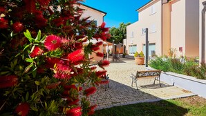 A courtyard with a paved walkway, a bench, and buildings with balconies. - Bolgheri Marina Resort ex Varo Village (Bibbona)