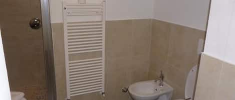 A bathroom with a shower, a towel rack, two bidets, and a toilet.