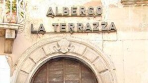 Rakennuksen sisäänkäynti, jonka yläpuolella on puinen ovi ja sen yläpuolella teksti ”ALBERGO LA TERRAZZA”.