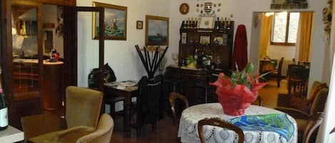 Comedor con una mesa preparada para cuatro personas, rodeada de sillas. Hay una araña colgando del techo, un cuadro en la pared y una ventana con cortinas.