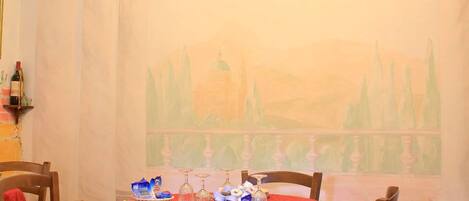 A dining area with a table set for four, wooden chairs, a chandelier, and a mural on the wall.