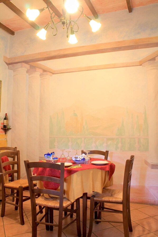 A dining area with a table set for four, wooden chairs, a chandelier, and a mural on the wall.