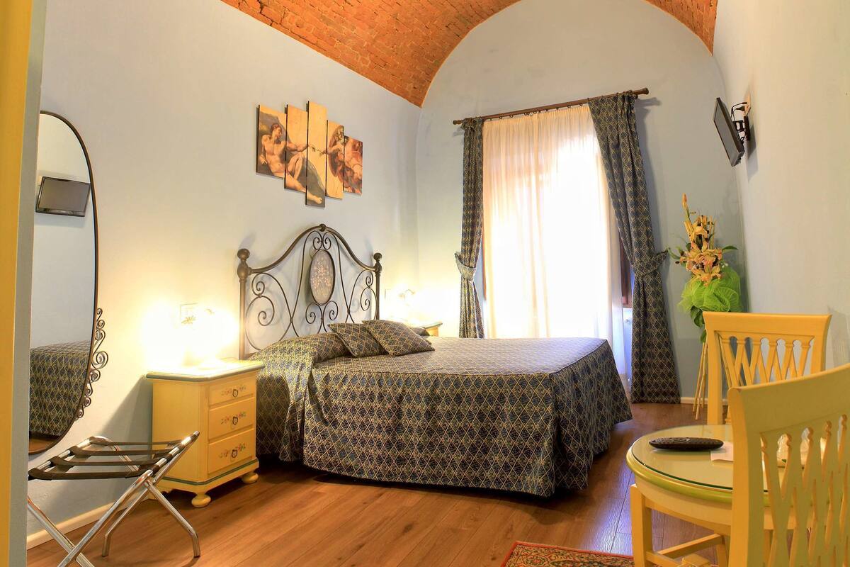 Ein Schlafzimmer mit Ziegeldecke, einem Bett mit gemusterten Textilien, einem Nachttisch, einem Sessel und einem kleinen Tisch mit Fernbedienung.