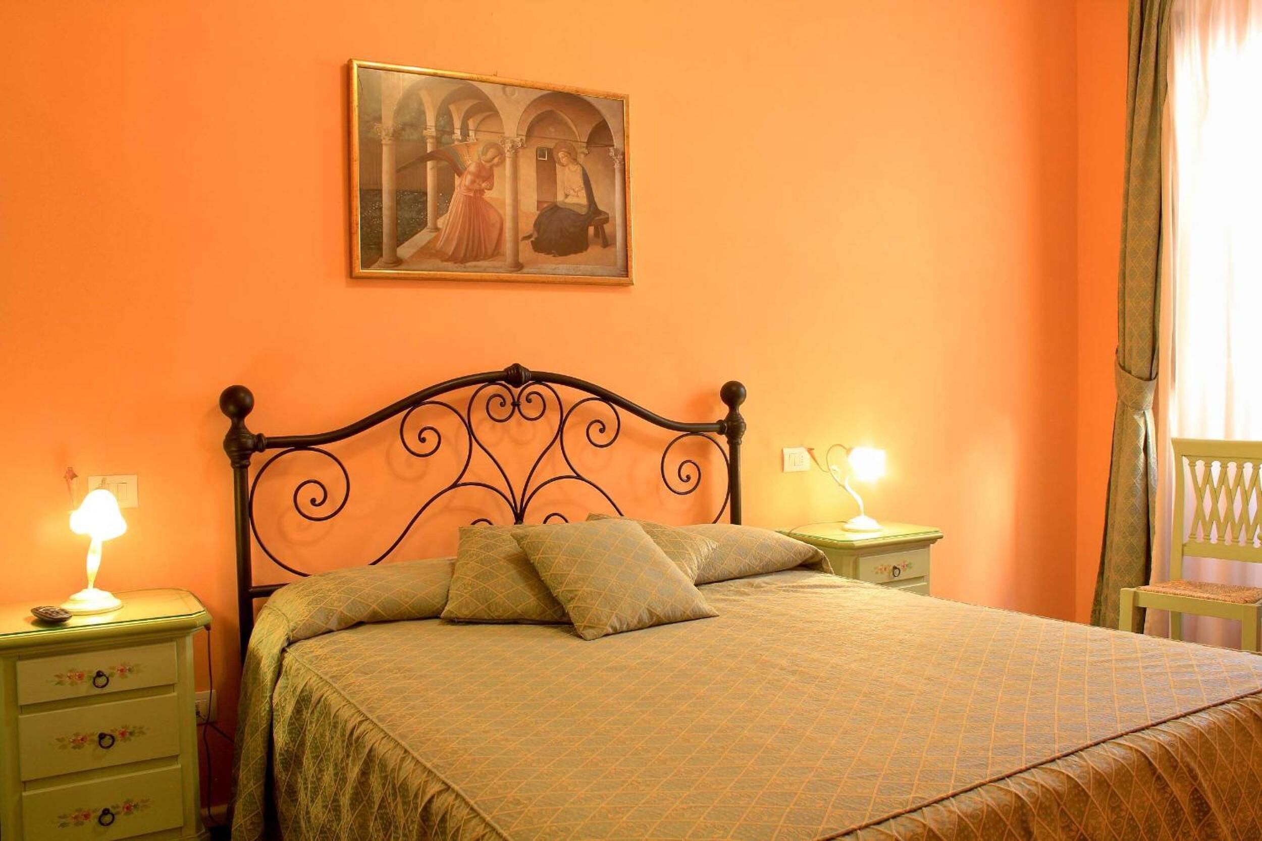 A bedroom with a bed, two bedside tables, a nightstand, a lamp, a painting, and a chair.