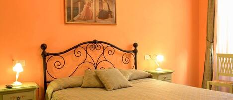A bedroom with a bed, two bedside tables, a nightstand, a lamp, a painting, and a chair.