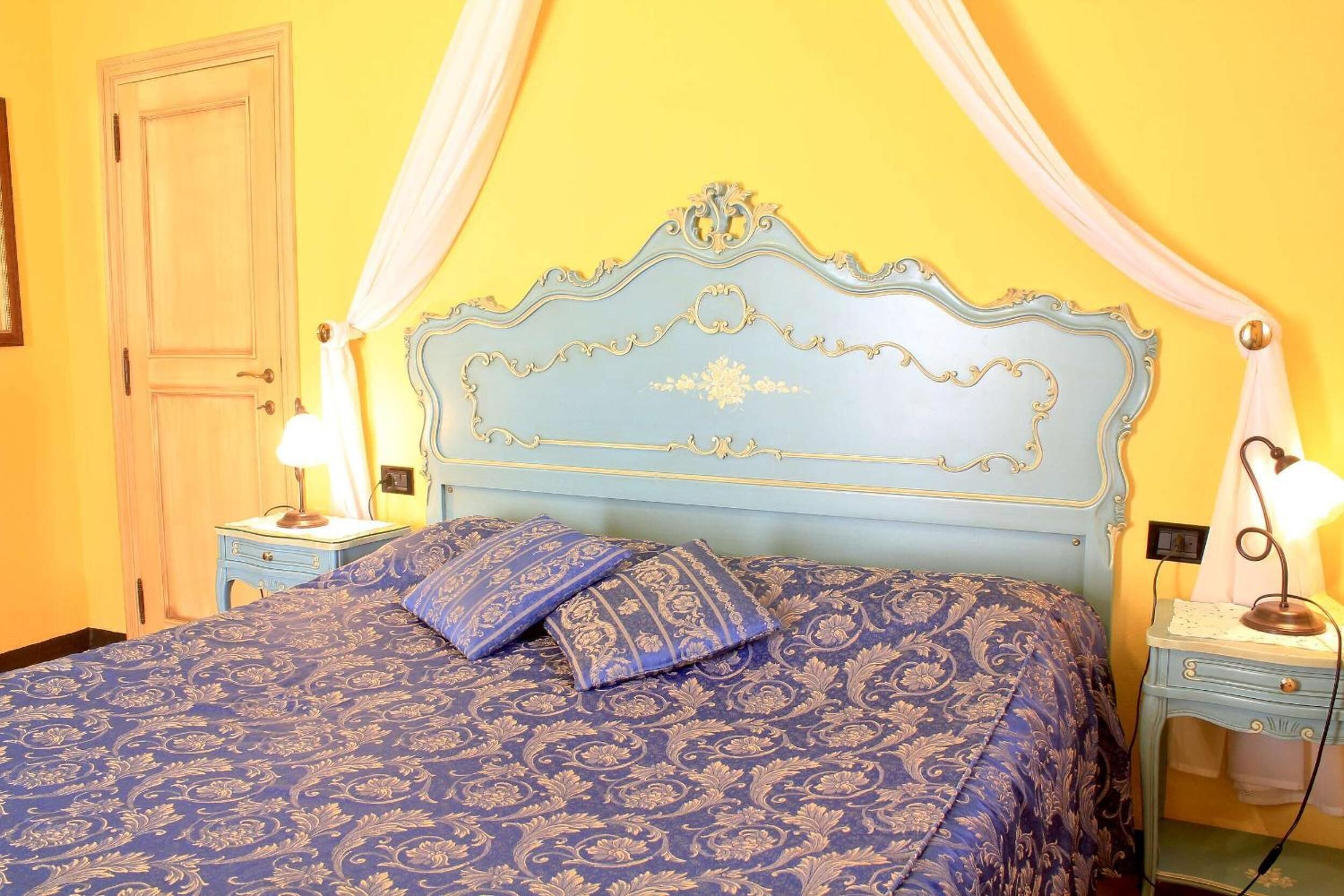 Un dormitorio con una colcha azul estampada, un cabecero decorativo y dos lámparas de noche.