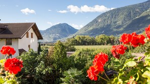 Una casa con techo inclinado, rodeada de abundante vegetación y montañas al fondo.