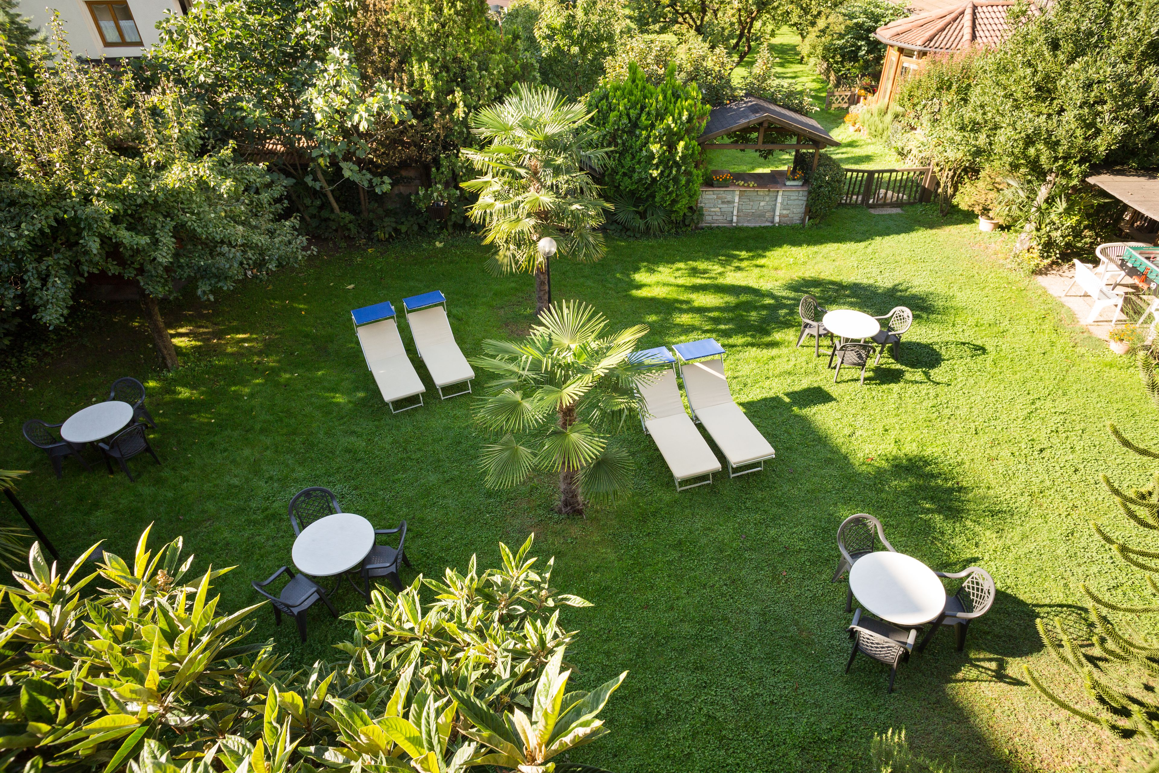 A well-maintained garden with multiple seating areas, including lounge chairs and tables, surrounded by lush greenery and trees.