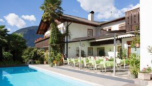 Zona de piscina con comedor, telón de fondo de montañas y un edificio con balcón.