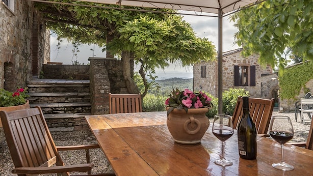 A rustic outdoor dining area with a wooden table, chairs, and a large vase of flowers. - Agriturismo La Palazzina (Murlo)