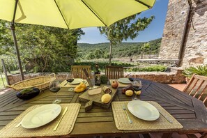 An outdoor dining table set with plates, cutlery, and a bottle of wine, under a yellow umbrella, with a scenic view of hills and a stone wall in the background. - Agriturismo La Palazzina (Murlo)
