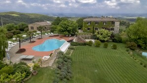 A large swimming pool with lounge chairs, a stone building, and a well-maintained lawn. - Agriturismo La Palazzina (Murlo)