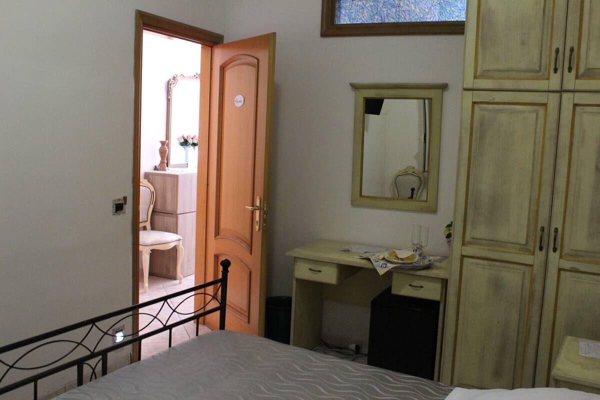A bedroom with a bed, a desk, a chair, a wardrobe, and a mirror.