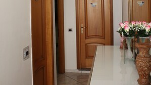 Un pasillo con puertas de madera, suelo de baldosas blancas y un florero con flores sobre una encimera blanca.