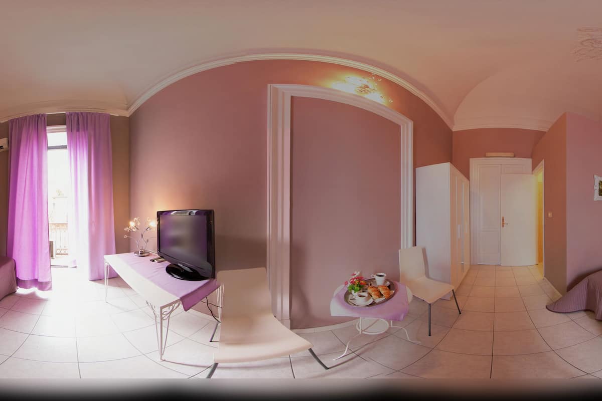 A modern hotel room with a large bed, a desk with a television, and a small table with a tray of breakfast.