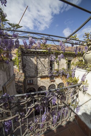 A balcony with a wrought iron railing, overlooking a courtyard with a building featuring arched windows and a tiled roof. - Hotel Biscari Catania (Catania)