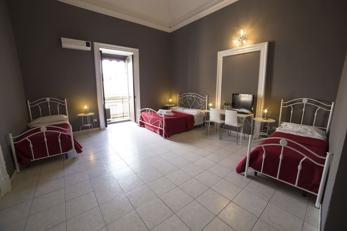 A hotel room with three beds, a desk, a TV, and a balcony.