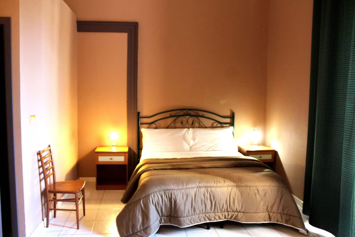 A bedroom with a single bed, two bedside tables, a chair, and a nightstand with lamps.