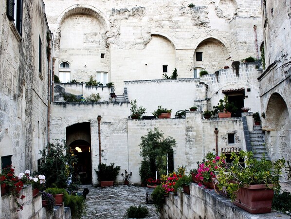A courtyard with stone walls, arched doorways, and potted plants. - Residenza le Dodici Lune (Matera)