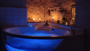 Un baño de spa con luz azul, velas y una pared de piedra.