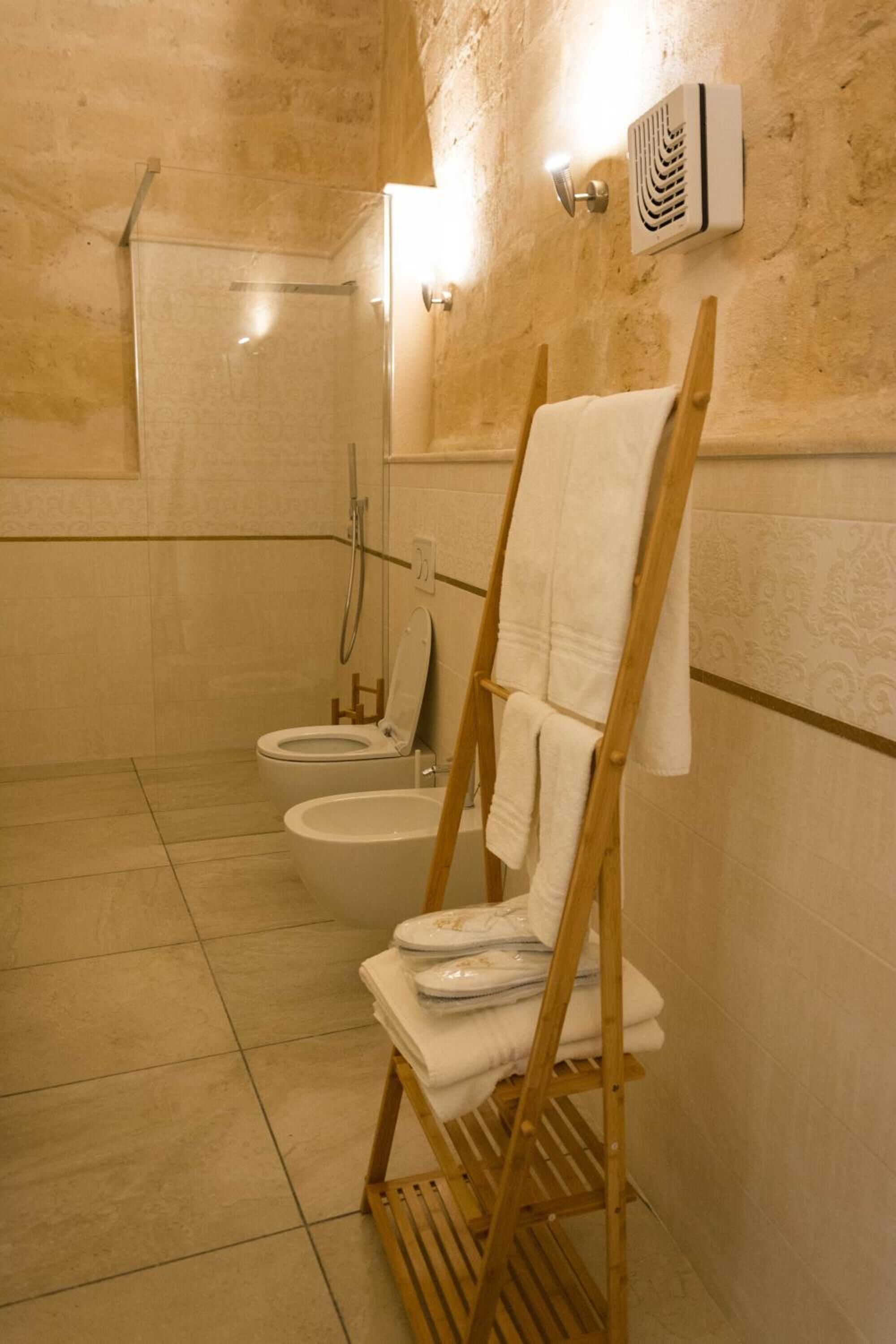Une salle de bain avec une douche, deux toilettes et un porte-serviettes en bois sur lequel sont pliées des serviettes.
