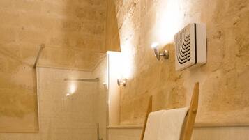 Une salle de bain avec une douche, deux toilettes et un porte-serviettes en bois sur lequel sont pliées des serviettes.
