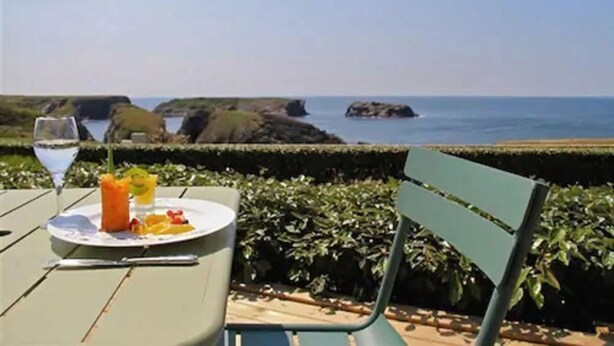 Una mesa con un plato de comida y una bebida, con vistas a un paisaje costero con rocas y el mar.