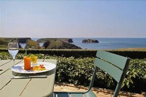 Une table avec une assiette de nourriture et une boisson, donnant sur un paysage côtier avec des rochers et la mer.