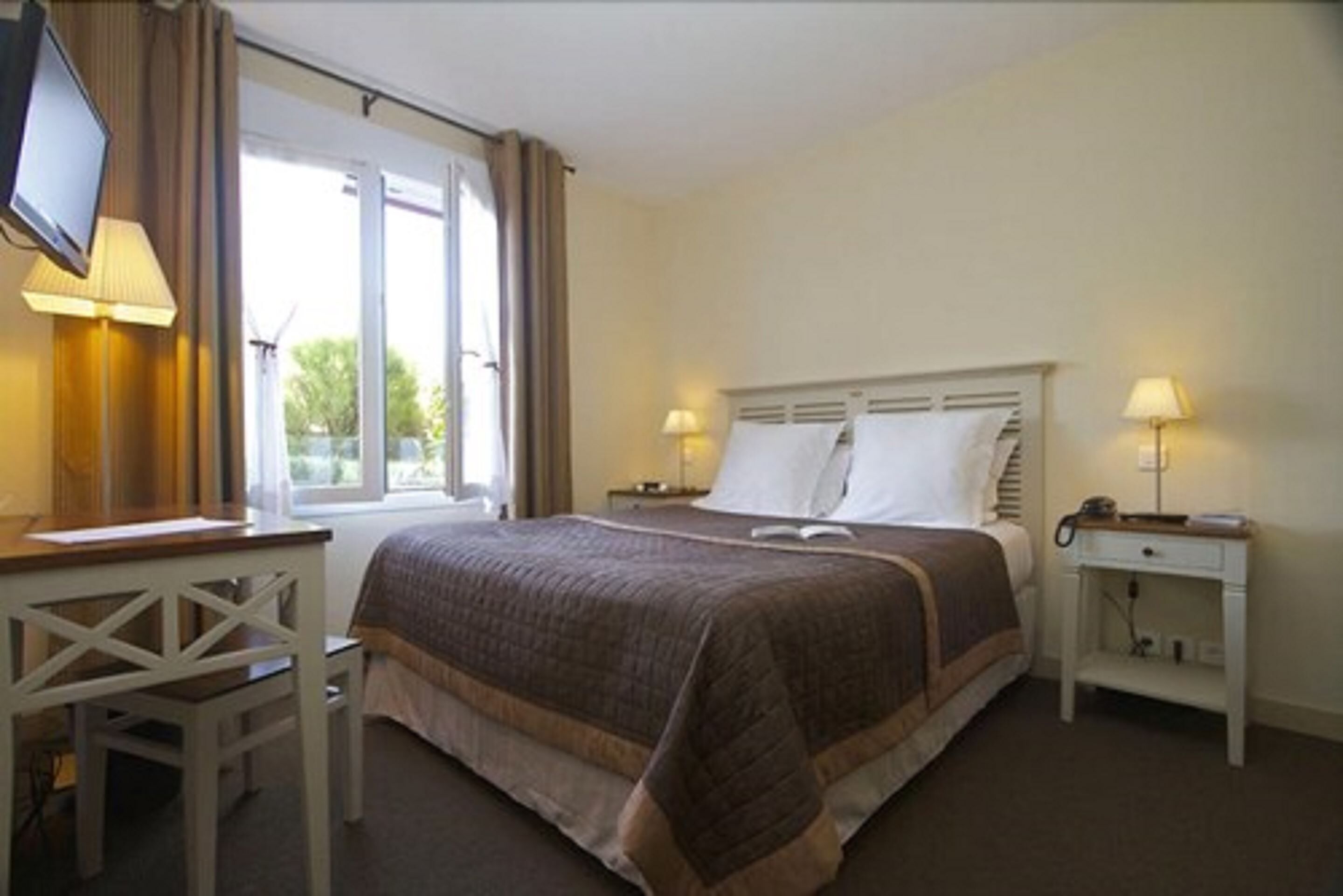 A hotel room with a bed, a desk, a chair, a TV, and two bedside lamps.