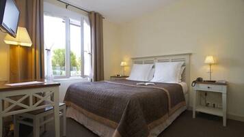A hotel room with a bed, a desk, a chair, a TV, and two bedside lamps.