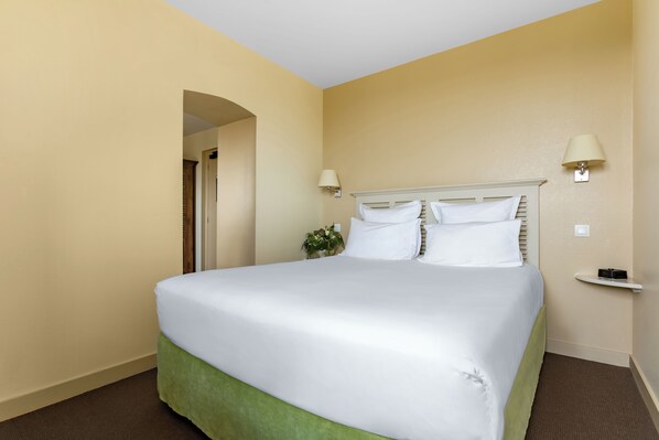 A hotel room with a large bed, two bedside lamps, a small table, and a potted plant.