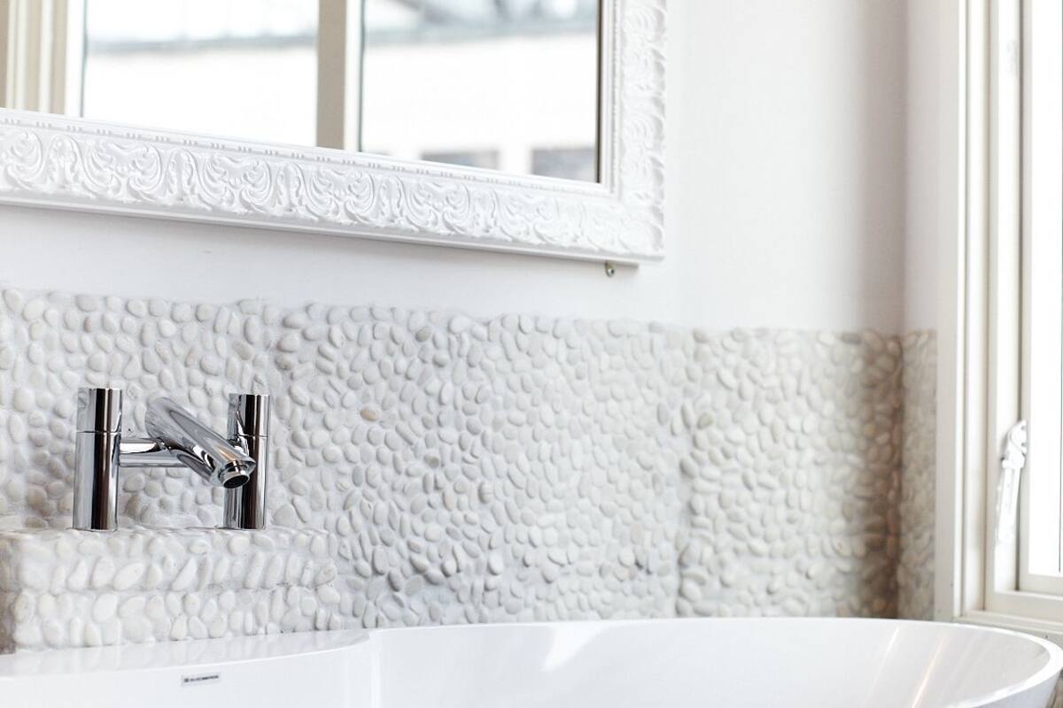 A bathroom with a freestanding bathtub, a white textured wall, and a mirror with a decorative frame.