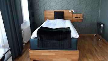 En säng med en sänggavel i trä, en vit kudde och ett mörkt täcke.