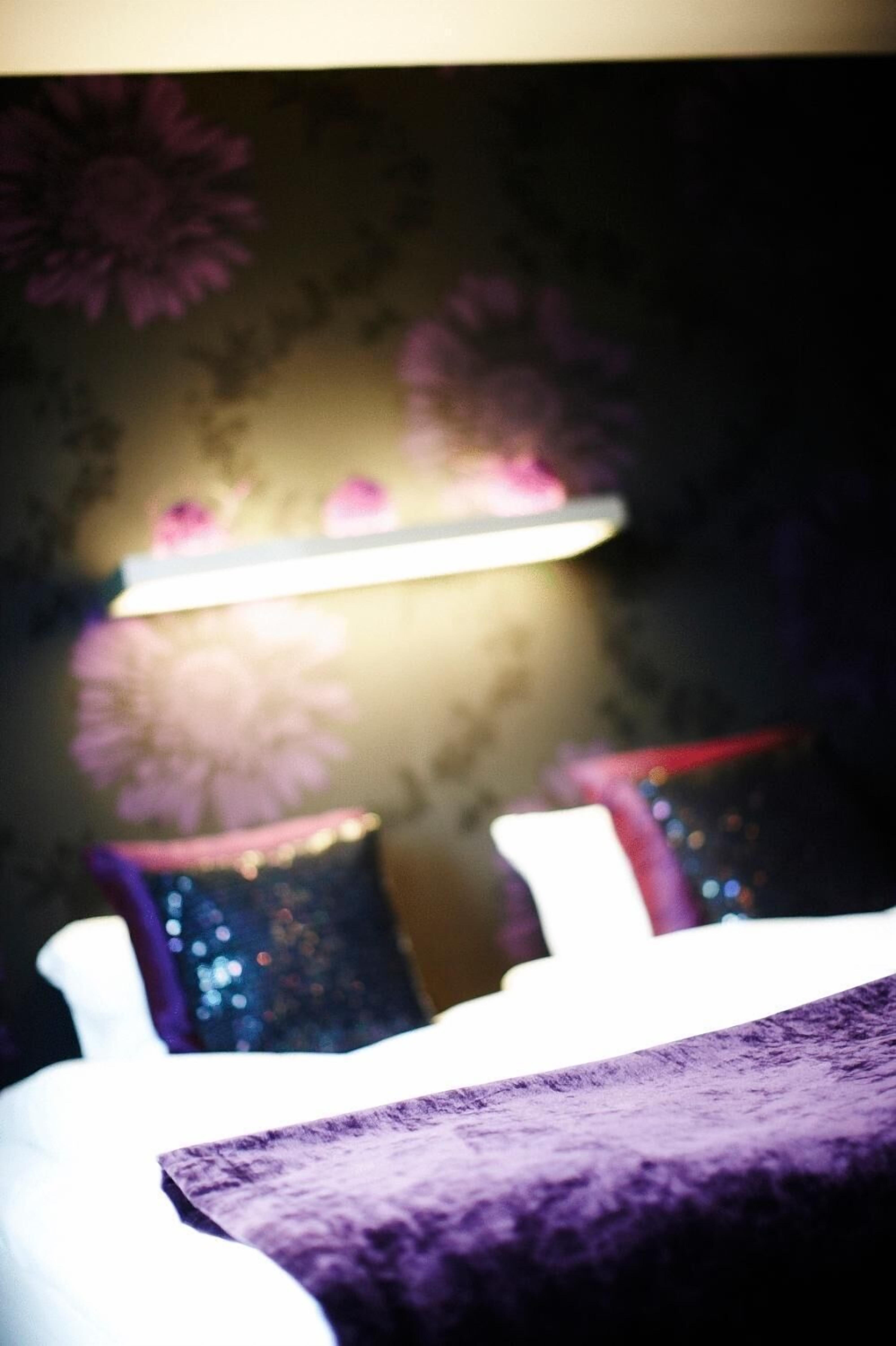 Ein Bett mit lila Bettdecke, eine Nachttischlampe und eine Wand mit floralem Wandpapier.