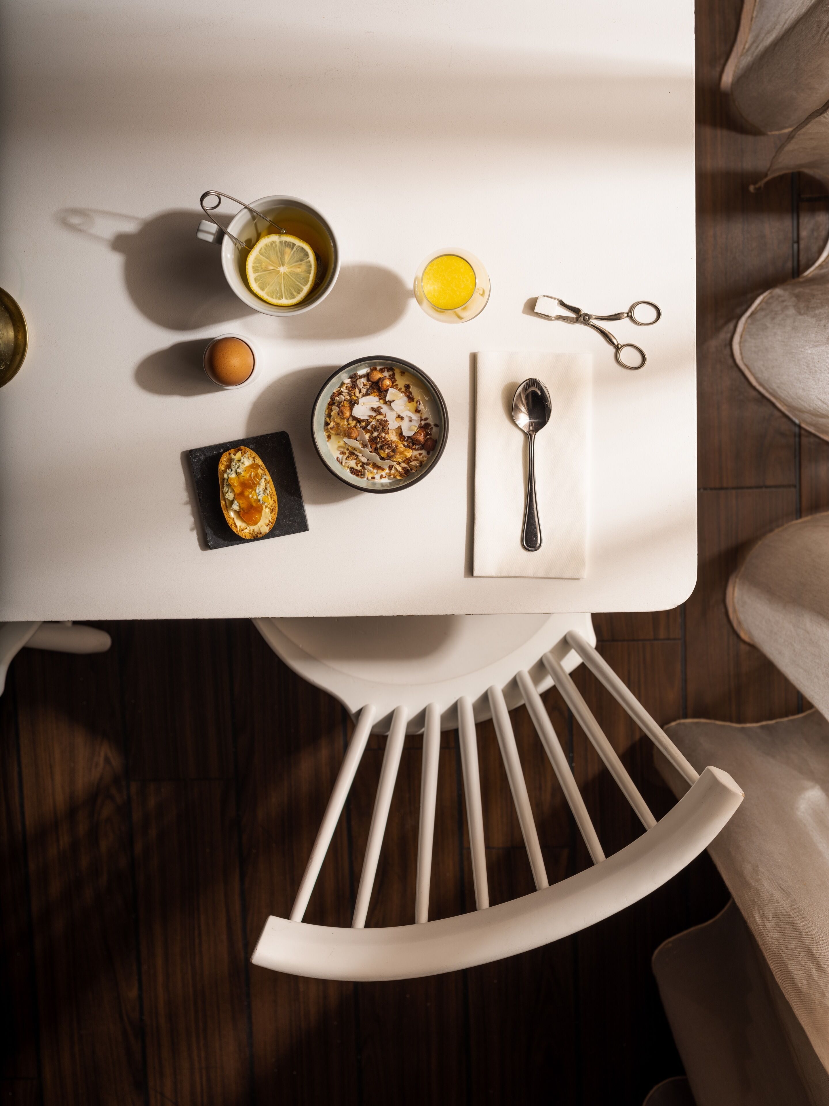 A breakfast setting with a bowl of cereal, a cup of coffee, a glass of orange juice, and a pair of scissors on a white table.