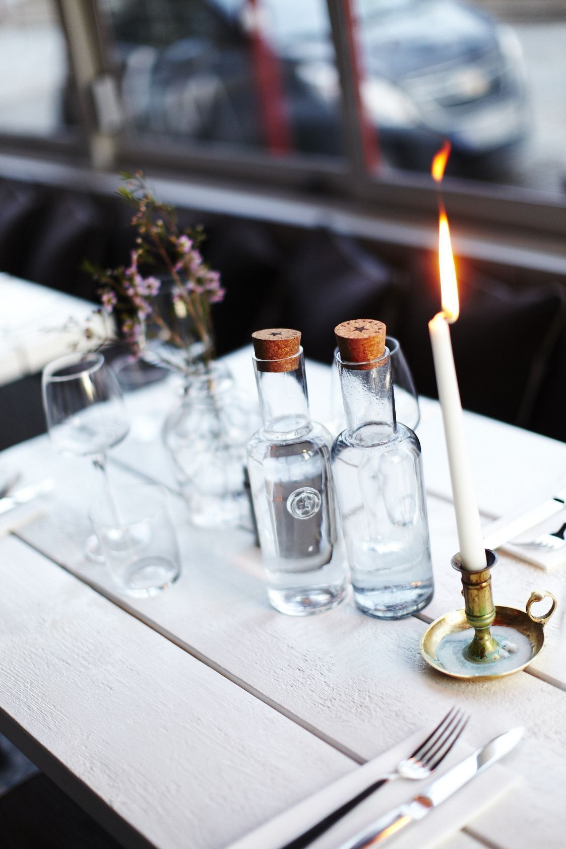 A table set with clear glass bottles, a lit candle, and a fork and knife.