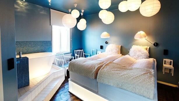 A modern bedroom with a large bed, a built-in bathtub, and multiple hanging light fixtures.