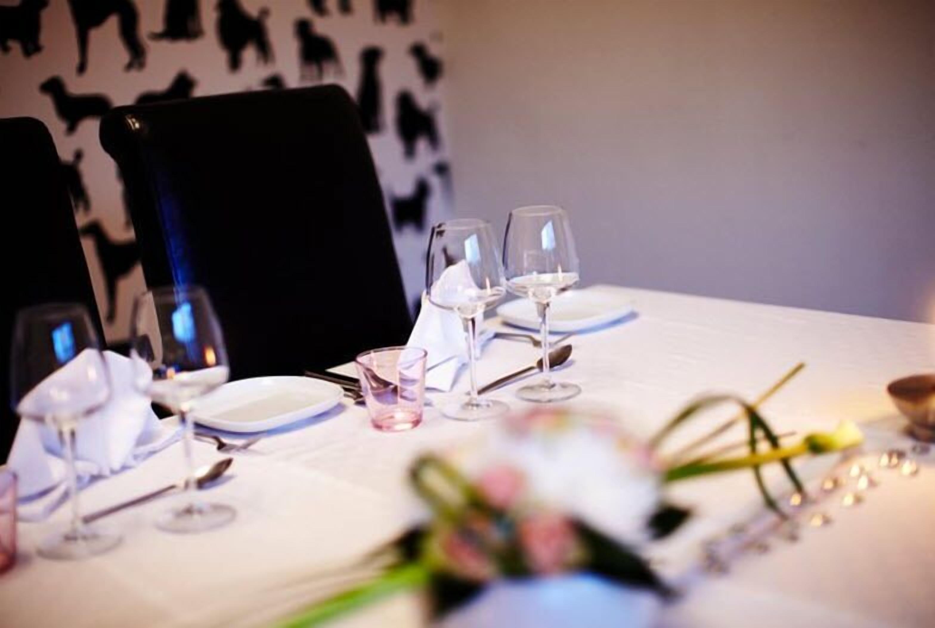 A dining table set with plates, glasses, and cutlery, with a floral arrangement in the foreground.